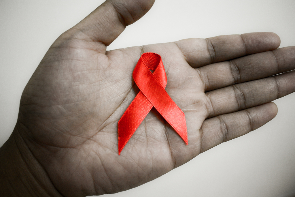 Mão segura um laço vermelho, símbolo de combate à Aids
