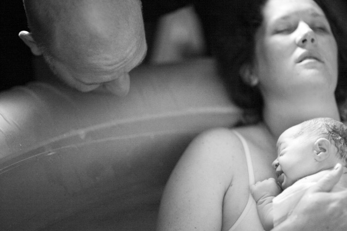 Mulher sentada em banheira com água segura bebê recém-nascido